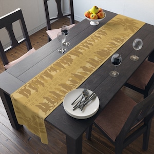 May include: A beige table runner with a palm tree design and the text "AND MOSES SAID UNTO THE PEOPLE, REMEMBER THIS DAY IN WHICH HE CAME FOR BY STRENGTH OF HAND THE LORD BROUGHT YOU OUT FROM THE" printed on it. The runner is on a dark brown wooden table with two chairs and a bowl of apples.