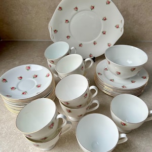 Könnte beinhalten: Eine weiße Keramik-Tasse mit schwarzem Henkel und dem Text "But First, Coffee" in fetter, schwarzer Schrift. Die Tasse steht vor einem verschwommenen Hintergrund, der eine gemütliche Umgebung suggeriert. Die Tasse ist etwa 10 cm hoch.