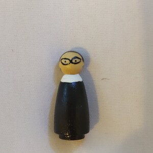 以下が含まれることがあります： 黒いローブと眼鏡をかけた人の木製の置物。置物は白い襟と黒い台座がついています。