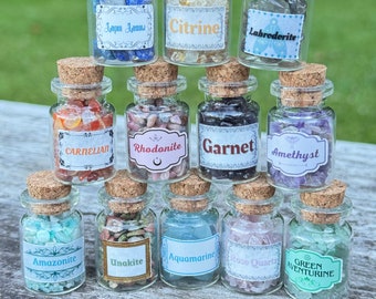 May include: A selection of small glass bottles with cork stoppers, each containing different gemstones. Labels identify the stones as Lapis Lazuli, Citrine, Labrodorite, Carnelian, Rhodonite, Garnet, Amethyst, Amazonite, Unakite, Aquamarine, Rose Quartz, and Green Aventurine.