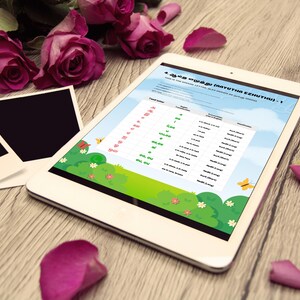 May include: A white tablet displaying a colorful educational chart with text in a foreign language. The tablet is surrounded by pink roses, photo frames, and rose petals on a wooden surface.