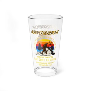 May include: A clear glass pint glass with a gold graphic of a Bigfoot-like creature standing on a mountain with a sunset behind it. The text reads "Sasquatch Ballet Performance Company Forest Theatre Bluff Creek, California Appearing One Day Only October 20, 1967".