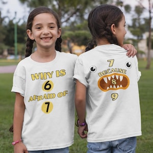 Könnte beinhalten: Zwei Kinder tragen weiße T-Shirts mit einem Mathe-Motiv. Das vordere Shirt sagt "WHY IS 6 AFRAID OF 7" mit gelben Zahlen. Das hintere Shirt sagt "7 BECAUSE 8 9" mit einer Monstergrafik.