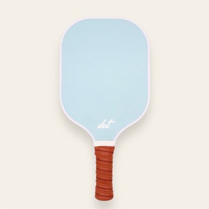 May include: A light blue paddleball racket with a white border and a brown leather grip. The paddle has the word "dot" written on it in white.