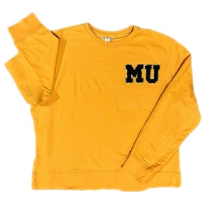 May include: A mustard yellow long-sleeved sweatshirt with a black felt "MU" patch on the left chest.