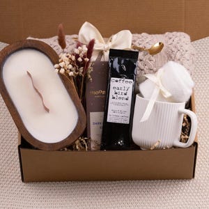 K&ouml;nnte beinhalten: Geschenkbox mit einer Holzkerze, Kaffee, einer Tasse und anderen Artikeln. Die Kerze befindet sich in einer Holzschale. Auf dem Kaffeebeutel steht "early bird blend". Die Tasse ist wei&szlig; mit vertikalen Linien.
