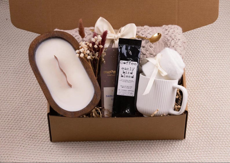 K&ouml;nnte beinhalten: Geschenkbox mit einer Holzkerze, Kaffee, einer Tasse und anderen Artikeln. Die Kerze befindet sich in einer Holzschale. Auf dem Kaffeebeutel steht "early bird blend". Die Tasse ist wei&szlig; mit vertikalen Linien.
