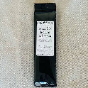 May include: Black coffee pouch with white text that reads "coffee early bird blend a five bean blend with excellent flavor & mild acidity Brews 8-10 cups 100% arabica la crema coffee www.lacremacoffeecompany.com west chester, oh 45069 net weight 1.5 oz./42.5 g"