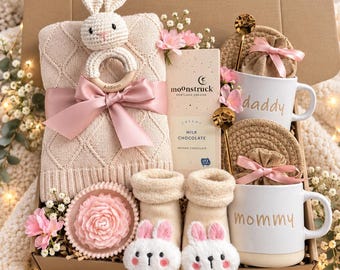 May include: A gift box containing a beige knit blanket with a pink ribbon, a crochet bunny rattle engraved with Addison, a Moonstruck milk chocolate bar, two white mugs labeled daddy and mommy, two gold spoons, and baby socks with bunny faces.