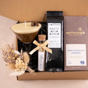 K&ouml;nnte beinhalten: Eine Geschenkbox mit Kaffee, Schokolade und einer Kerze. Die Kerze befindet sich in einem Martiniglas und ist mit Schokoladenquadraten belegt. Ein kleines Fl&auml;schchen Streichh&ouml;lzer und ein Strau&szlig; Trockenblumen sind ebenfalls enthalten. Auf dem Kaffeesack steht "early bird blend".