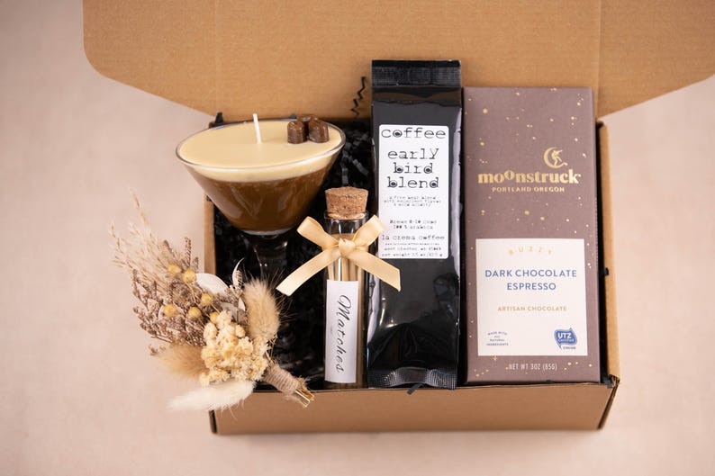 K&ouml;nnte beinhalten: Eine Geschenkbox mit Kaffee, Schokolade und einer Kerze. Die Kerze befindet sich in einem Martiniglas und ist mit Schokoladenquadraten belegt. Ein kleines Fl&auml;schchen Streichh&ouml;lzer und ein Strau&szlig; Trockenblumen sind ebenfalls enthalten. Auf dem Kaffeesack steht "early bird blend".