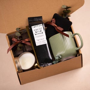 K&ouml;nnte beinhalten: Geschenkbox mit einer gr&uuml;nen Tasse, schwarzem Kaffee, einer Kerze und Schokolade. Die Tasse hat vertikale Rillen. Auf dem Kaffeebeutel steht "early bird blend". Die Box ist mit einem braunen Band gebunden.