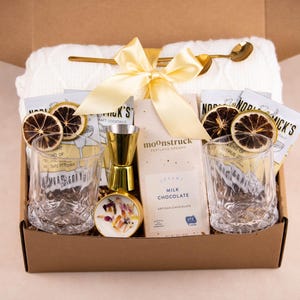 May include: A gift box filled with cocktail-themed items. Includes two etched glasses, a gold-colored jigger, a small bottle, a bar spoon, and a bar towel. Also includes chocolate and dried citrus garnishes.