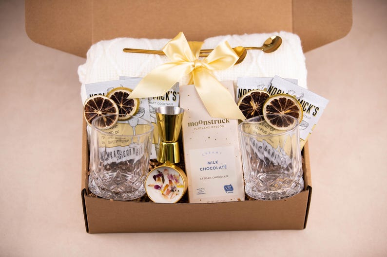 May include: A gift box filled with cocktail-themed items. Includes two etched glasses, a gold-colored jigger, a small bottle, a bar spoon, and a bar towel. Also includes chocolate and dried citrus garnishes.