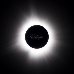 Pode incluir: Uma imagem marcante de um eclipse solar, apresentando um disco central escuro rodeado por uma coroa brilhante e radiante. A imagem é contra um fundo preto, com a assinatura do fotógrafo no centro.