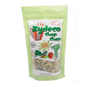 May include: A green resealable bag with a white label. The label has a red and white accordion design with the text "Zydeco Chop Chop". The label also has the text "All Natural, No Salt Added, Gluten Free" and "Great in all Foods!" with a green starburst design. The bag contains a blend of dried herbs and vegetables. The bag is labeled "Net Wt. 8 oz. (227g)".