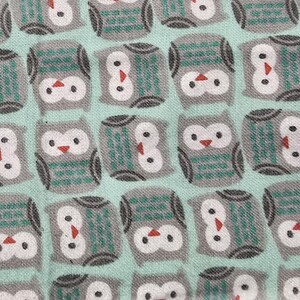 May include: Close-up of a fabric with a repeating pattern of stylized owls. The owls are gray with white faces, teal accents, and red beaks, set against a light teal background. The fabric appears to be cotton or a similar material.