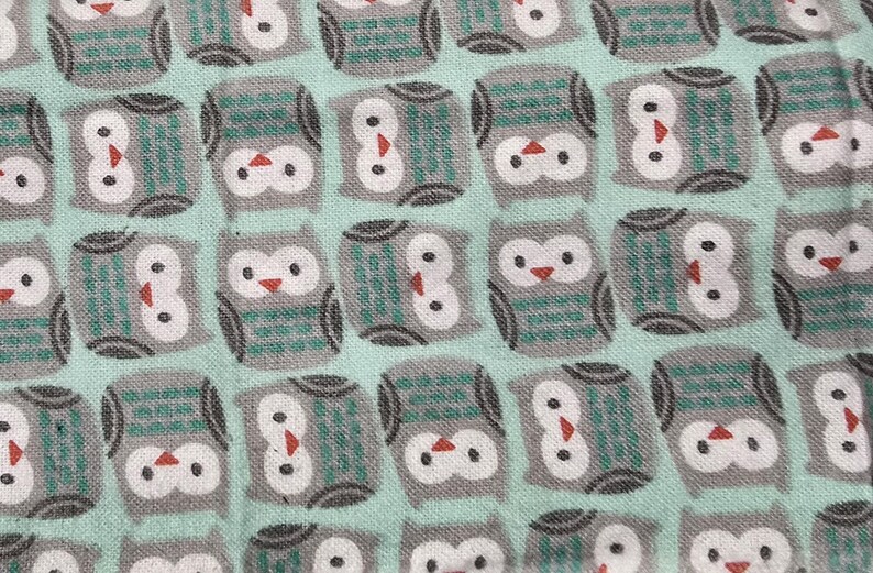 May include: Close-up of a fabric with a repeating pattern of stylized owls. The owls are gray with white faces, teal accents, and red beaks, set against a light teal background. The fabric appears to be cotton or a similar material.
