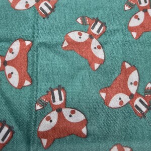 May include: Teal fabric with a repeating pattern of cartoon foxes in red, white, and black. The foxes have white faces, red bodies, and black and white striped tails. The fabric has a textured appearance.