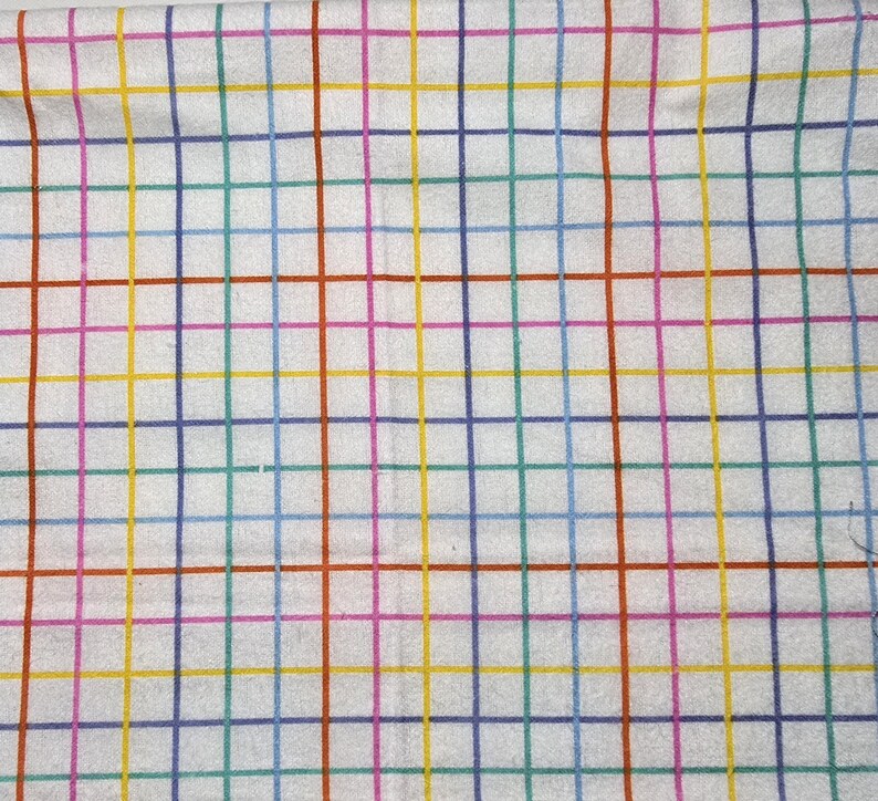 May include: White fabric with a colorful grid pattern. The grid lines are in various colors, including red, blue, green, yellow, and purple. The fabric appears to be soft and possibly cotton or linen.