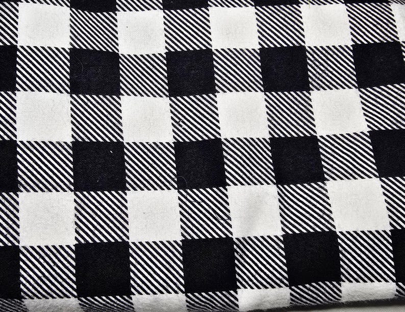 May include: Close-up of a black and white checkered fabric. The pattern consists of alternating squares of solid black and white, with diagonal lines filling some of the black squares. The fabric appears to be soft and possibly used for clothing or home decor.