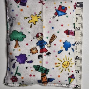 May include: A white rectangular pillow with a colorful print of crayons, baseball, a tree, and a smiling sun. The pillow is approximately 5 inches long.