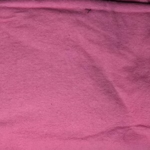 May include: A close-up shot of a textured, pink fabric. The fabric has a slightly uneven surface, with subtle variations in color and texture. The overall appearance is soft and inviting, with a warm, rosy hue.