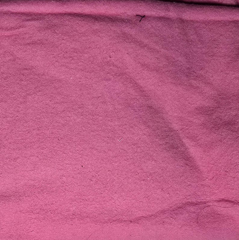 May include: A close-up shot of a textured, pink fabric. The fabric has a slightly uneven surface, with subtle variations in color and texture. The overall appearance is soft and inviting, with a warm, rosy hue.