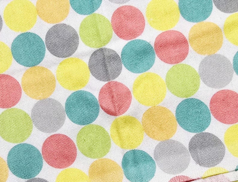 May include: Close-up of a white fabric with a repeating pattern of large, colorful polka dots. The dots are in shades of yellow, pink, green, blue, and gray. The fabric appears to be soft and textured.