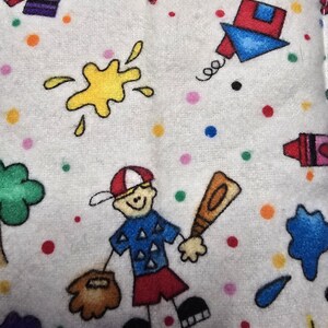 May include: White fabric with colorful illustrations of a baseball player, crayons, paint splatters, and a kite. The design includes a baseball player holding a bat and glove, surrounded by polka dots.