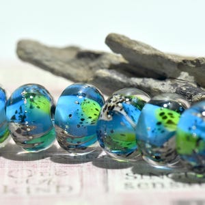 May include: Six glass beads with a blue, green, and white marbled pattern. The beads are round and have a glossy finish.