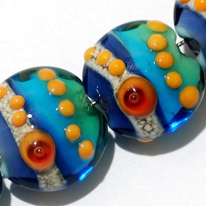 May include: A string of colorful glass beads with blue, green, orange, and white swirls and dots. The beads are round and have a glossy finish.