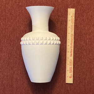 May include: White ceramic vase with a textured surface and a band of raised geometric shapes around the middle. The vase is approximately 10 inches tall.