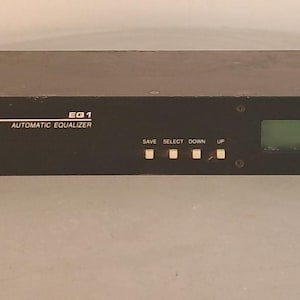 May include: A black Lectrosonics, Inc. EQ1 automatic equalizer rack-mount unit. The front panel features a green digital display screen, four small square control buttons labeled Save, Select, Down, and Up, and a power switch on the right side.