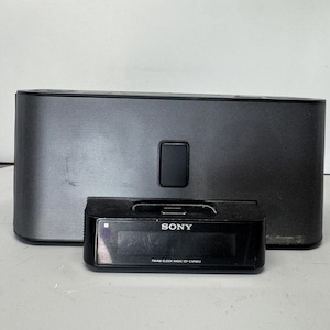 May include: A black Sony FM/AM clock radio model ICF-C1IPMK2 featuring a rectangular speaker unit with a mesh grille and a separate smaller black base unit with a digital display screen and a docking port for electronic devices.
