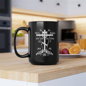 May include: Black ceramic coffee mug with a white graphic of a cross with Cyrillic text. The text reads "IC XC СНЪ БЖИЙ ЦРЬ НИ КА САВЫ МА РБ Γ Δ".