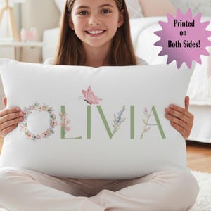 May include: White rectangular pillow with the name "OLIVIA" in green letters, adorned with floral and butterfly illustrations. The pillow has the text "Printed on Both Sides!" in a pink starburst.