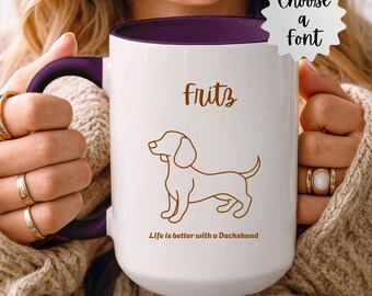 Op de afbeelding: Witte keramische mok met een paars interieur en handvat. De mok heeft een bruine teckel illustratie en de naam "Fritz" in een scriptlettertype. De tekst "Life is better with a Dachshund" wordt ook weergegeven.