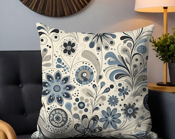 May include: Square throw pillow with a floral pattern in shades of blue, gray, and cream. The design features stylized flowers, leaves, and swirls. The pillow is placed on a dark gray couch.
