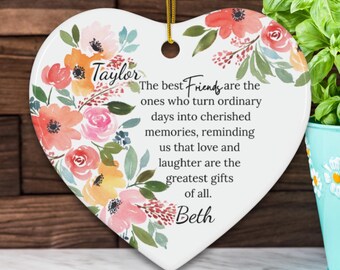 May include: Heart-shaped ceramic ornament with floral watercolor design in shades of orange, pink, and yellow. The ornament has the names "Taylor" and "Beth" and a quote about friendship.
