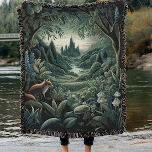 Può includere: Coperta in tessuto arazzo raffigurante una scena di foresta con un castello, una volpe e una vegetazione lussureggiante. La coperta ha uno sfondo scuro con un design paesaggistico dettagliato e bordi sfrangiati. La tavolozza dei colori include sfumature di verde, marrone e arancione.