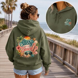 May include: An olive green hooded sweatshirt featuring a large graphic on the back with the text Salty as a Beach, palm trees, hibiscus flowers, seashells, sunglasses, and flip-flops. A smaller matching graphic is on the front chest.