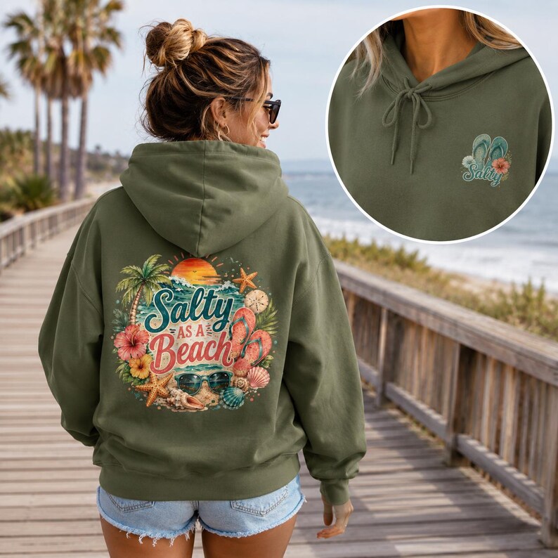May include: An olive green hooded sweatshirt featuring a large graphic on the back with the text Salty as a Beach, palm trees, hibiscus flowers, seashells, sunglasses, and flip-flops. A smaller matching graphic is on the front chest.