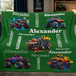 Op de afbeelding: Een groene deken met kleurrijke monstertrucks en de naam "Alexander" in het wit. De deken heeft een herhalend patroon van monstertrucks in verschillende kleuren, met de naam "Alexander" verticaal en horizontaal gedrukt.