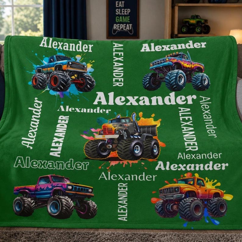 Op de afbeelding: Een groene deken met kleurrijke monstertrucks en de naam "Alexander" in het wit. De deken heeft een herhalend patroon van monstertrucks in verschillende kleuren, met de naam "Alexander" verticaal en horizontaal gedrukt.