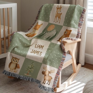 May include: A green and cream-colored baby blanket with a woodland animal theme, draped over a wooden rocking chair. The blanket features a repeating pattern of forest animals, trees, and the text "LIAM JAMES". The blanket has a fringed edge.