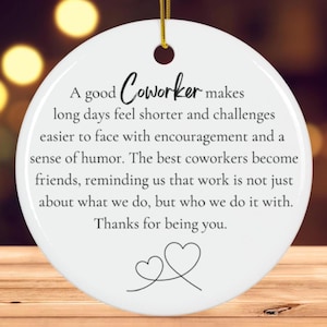 Peut inclure: Ornement rond en céramique blanche avec une ficelle dorée. Le texte "A good Coworker makes long days feel shorter..." est écrit en noir. Comprend deux cœurs entrelacés. Idéal pour les collègues.