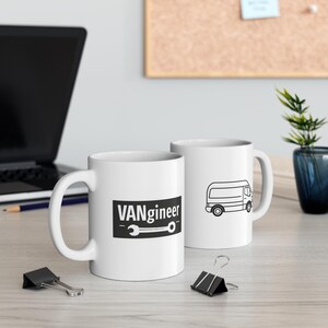 May include: Two white ceramic mugs. One mug features the text "VANgineer" in a black rectangle with a wrench graphic. The other mug has a black line drawing of a van. Both mugs have a white handle.