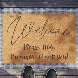May include: A brown welcome mat with a white and gray checkered border. The mat has the text "Welcome, Please Hide Packages - Thank you!" printed on it. A pair of black shoes are standing on the mat.