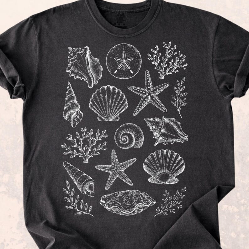 Puede incluir: Camiseta negra con una ilustraci&oacute;n blanca de varias conchas marinas, estrellas de mar y corales. El dise&ntilde;o presenta dibujos detallados de diferentes criaturas marinas, creando un tema costero.